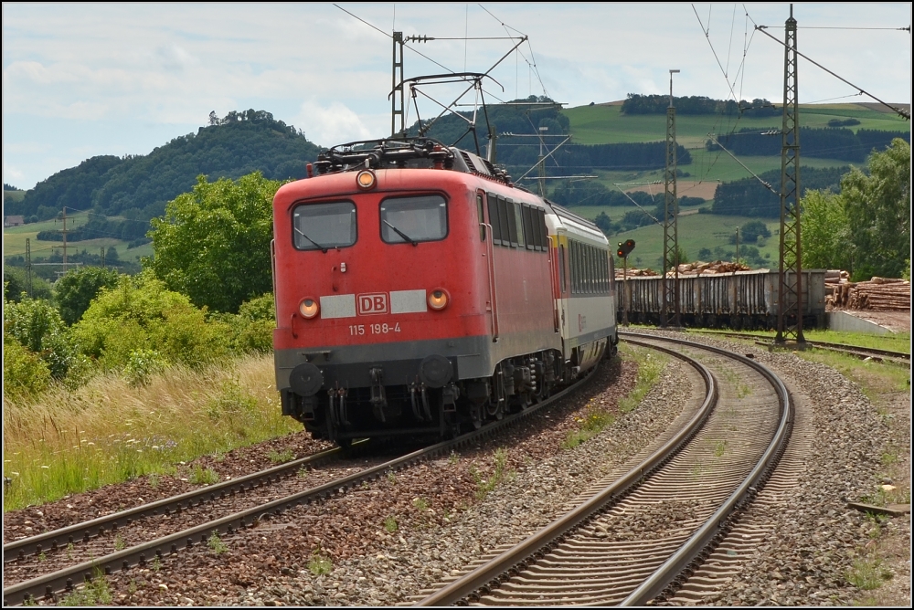 Sommertag im Hegau. Zum Schluss gab es noch Erlesenes. Hier durfte wie in alten Tagen wieder mal eine  110er  ihre Tatkraft unter Beweis stellen. 115 198 qult sich mit einem IC gleich die Engener Steige hinauf zur Wasserscheide. Hier fhrt die Gubahn noch auf den Gleisen der Schwarzwaldbahn. Im Hintergrund der eher unscheinbare Mgdeberg, wie alle anderen Hegauvulkane auch von einer Burgruine gekrnt. Welschingen im Juli 2012. Irgendwie sortiert sich das Bild nur widerwillig in die Kategorie Baureihe 115...