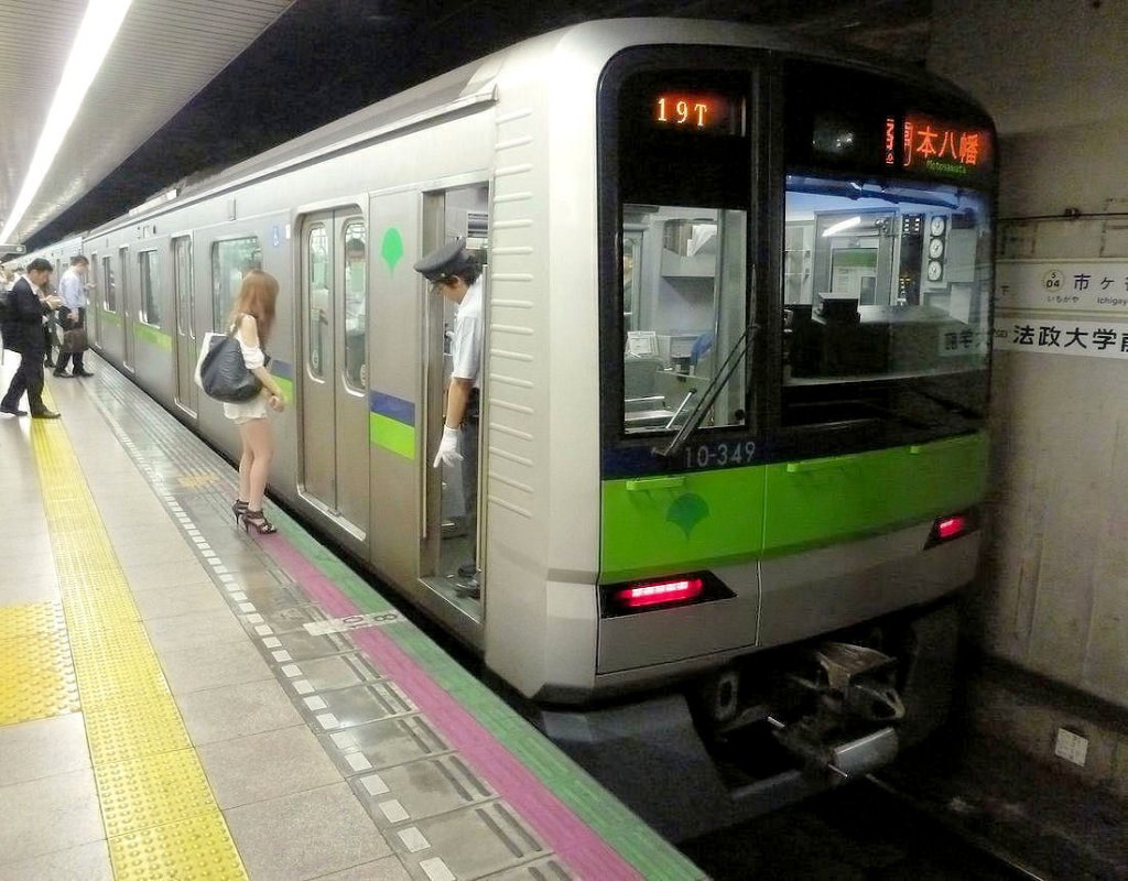 Städtische U-Bahn Tokyo, Shinjuku-Linie, neue Wagen: Zur Bildung neuer Züge und von 10- statt 8-Wagenzügen wurden 2004-2006 108 neue Wagen beschafft. Zug 10-340 (Endwagen 10-349) im Bild hat an beiden Enden einen neuen Steuerwagen. Ichigaya, 24.Juni 2011. Den Menschen zuzuschauen macht immer Spass: Bevor der Schaffner die Türen öffnet, kontrolliert er, ob der Zug millimetergenau am Bahnsteig angehalten hat. Nicht so genau dagegen nimmt es die Dame, die die Regel missachtet, bei der Zugseinfahrt hinter der gelben Linie zu warten. 

