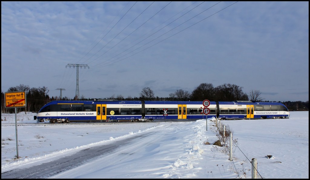 Starker Wind hat fr die Schneeverwehungen im Vordergrund gesorgt das man kaum noch die Strae sehen kann als OLA VT 0004 den Bahnbergang bei Torgelow am 11.03.13 passiert!