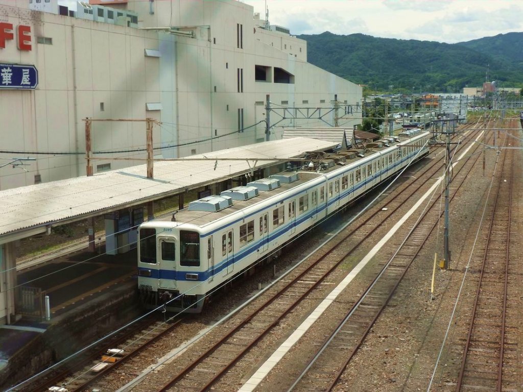 Tôbu Serie 8000, der klassische Tôbu-Lokalverkehrszug mit Längssitzen: 1963 bis 1983 wurden 712 Wagen gebaut; heute sind noch rund 500 Wagen im Einsatz, die meisten modernisiert. Es gibt diesen Typ als 2-,3-,4-,6- und 8-Wagenzug. Im Bild Zug 8199 in Yorii, einem Städtchen 75km vom Ausgangspunkt in Tokyo entfernt, 24.Juni 2011. (Aufnahme durch ein vergittertes Fenster)