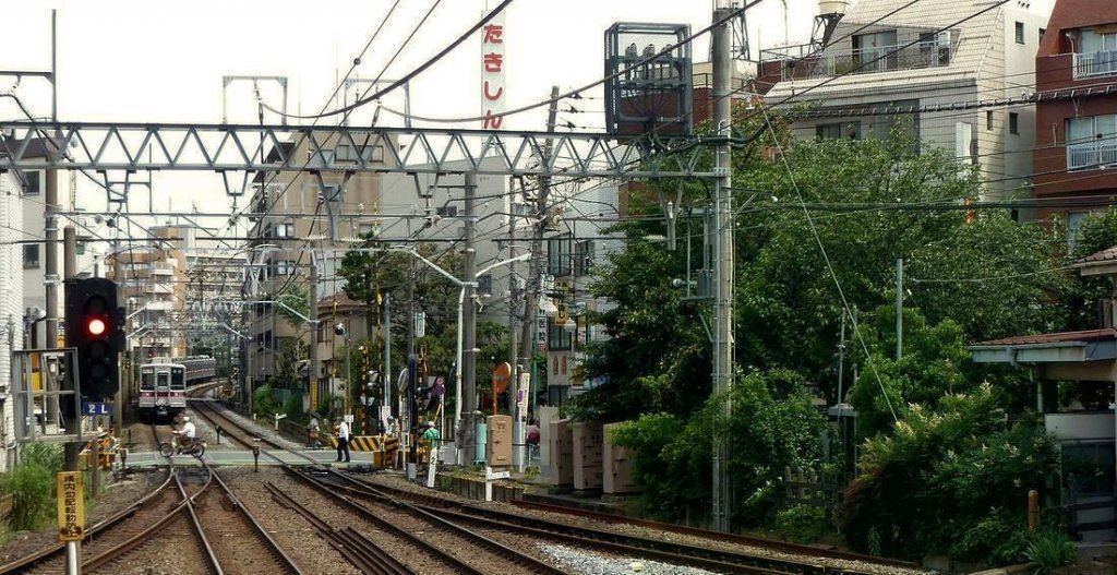 Tbu-Konzern Serie 1xxxx - Einfahrt nach Tokyo: Der Zugsverkehr ist ungeheuer dicht; kaum hat der 10-Wagenzug (6+4-Wagenzug, Zug 11452 an hinterer Stelle) den Bahnbergang freigegeben, brummen einige Motorrder darber, bevor sich in wenigen Sekunden die Schranke wieder schliesst. Naka Itabashi, 24.Juni 2011.  