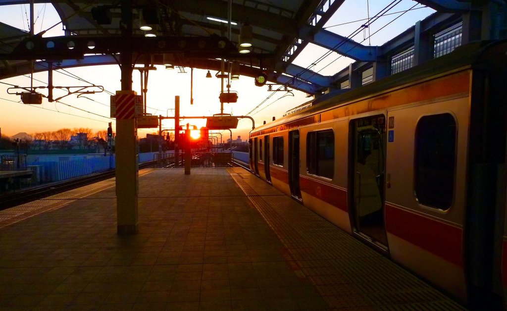 Tokyo S-Bahn, Serie 233: Tokyo-Higashi Koganei bei Sonnenuntergang. Links am Bildrand ist der Fuji-Berg zu sehen - an einem klaren Tag immer ein grossartiges Erlebnis. Soeben ist ein Zug der S-Bahn Chûô-Linie (mit Steuerwagen KUHA 232-22) eingetroffen; er steht bereit zur Weiterfahrt nach Tokyo Hauptbahnhof. 12.März 2013. CHÛÔ-LINIE 
