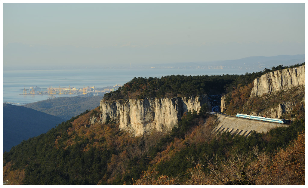 Triebwagen der SZ Baureihe 310 am 12.12.12 auf der Koperrampe kurz vor dem Bahnhof Črnotiče aufgenommen. Im Hintergrund sind Teile der Hafenanlage Triest zu sehen.
