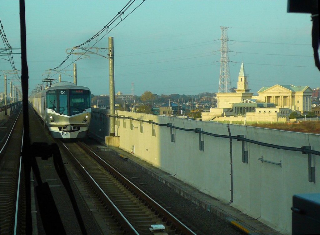 Tsukuba Express Serie 1101: Zug 1112 fhrt in Kashiwa-no-ha Campus ein. Von der Abendsonne beschienen die rtliche Hochzeitszeremonienhalle. 25.November 2009. 