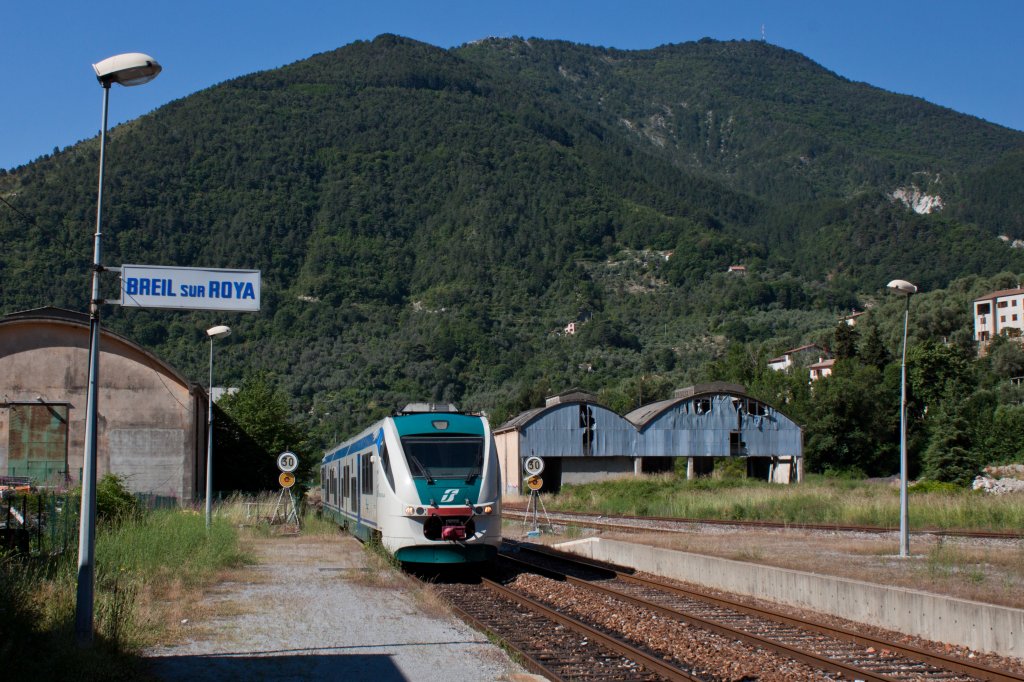 Und weiter geht's: Der ALn 501 037 trifft als R 22964 (Ventimiglia > Cuneo) in Breil-sur-Roya ein. 
Derzeit bilden diese im Zweistundentakt fahrenden Triebzge der Trenitalia das Grundangebot auf der internationalen Tendalinie zwischen der Cte d'Azur und dem Piemont. Auf der Zweigstrecke nach Nice fahren in unregelmssigen Abstnden Regionalzge der SNCF, die teilweise unter dem Marketingnamen  Train des Merveilles  weiter bis nach Tende verkehren. 
Die hier zu sehenden verfallenden Anlagen sind Zeugen einer Zeit, als der Tendabahn noch eine weit grssere Bedeutung zukam. Aktuell ist die erst 1979 reaktivierte und usserst spektakulr angelegte Strecke von einer erneuten Einstellung bedroht, wogegen sich die Anlieger aus dem Piemont, Ligurien und dem franzsischen Dpartement Alpes-Maritimes noch zu wehren wissen. Auch die Auslastung der Zge schien mir zumindest auf dem Hauptast nach Ventimiglia alles andere als schlecht. 
Breil-sur-Roya, Rgion PACA am 14. Juni 2013