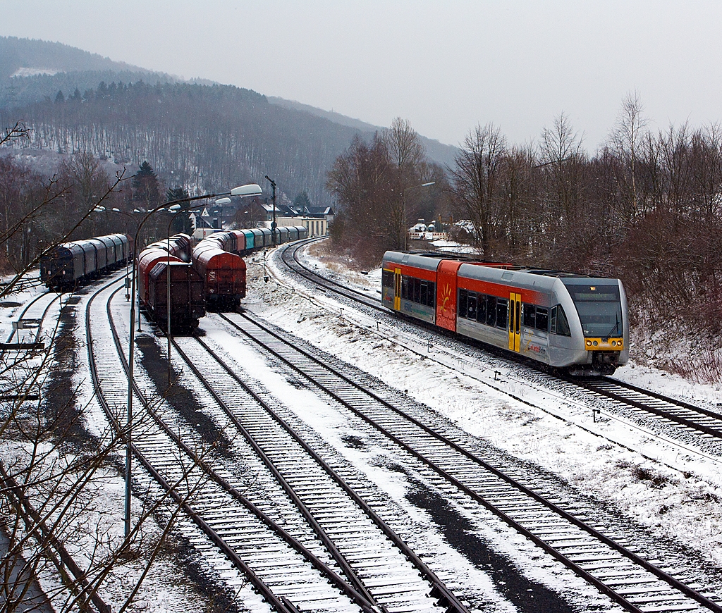 Und wieder, wie mein Freund Stefan es nennt, lsst der Winter seinen Abfall fallen – 
Ein Stadler GTW 2/6 der Hellertalbahn kommt ber gleichnamentlichen Hellertalbahn (KBS 462), bei leichten Schneefall, von Neunkirchen und erreicht gleich den Bahnhof Herdorf, von wo er dann weiter in Richtung Betzdorf/Sieg fhrt. 

Links auf dem Rangierbahnhof der KSW Kreisbahn Siegen-Wittgenstein (ehem. Freien Grunder Eisenbahn AG), sind wieder sehr viele Schiebeplanenwagen fr Coiltransporte der Gattung Shimmns abgestellt, hier ist aber Sonntagsruhe.
