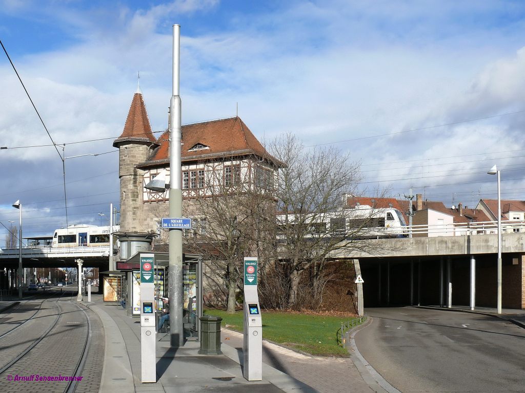 Unten ist die Straßenbahnhaltestelle Krimmeri in Straßburg-Neudorf am Weichenstellplatz = Square de l´Aiguillage. Oben auf der Eisenbahn befindet sich der Haltepunkt Krimmeri-Meinau. Hinter dem alten Stellwerk fahren die OSB VT509+VT512 als Zug OSB87429 von Strasbourg über Kehl nach Offenburg.

2012-12-30 Strasbourg Krimmeri
