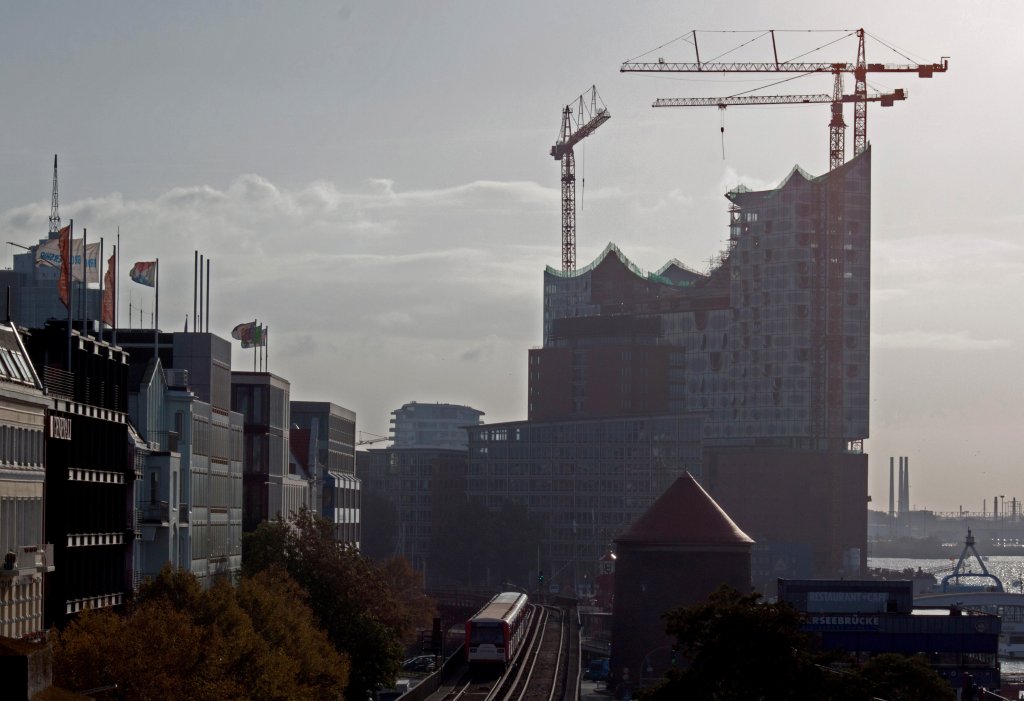 Voll gegen die gerade erst aufgegangene Morgensonne: Ein Zug der U3 fhrt vor dem Hintergrund der sich im Bau befindlichen Elbphilharmonie zwischen den Stationen Baumwall und Landungsbrcken dem sich vom Nebel befreienden Hamburger Hafen entlang. (19.Oktober 2011)