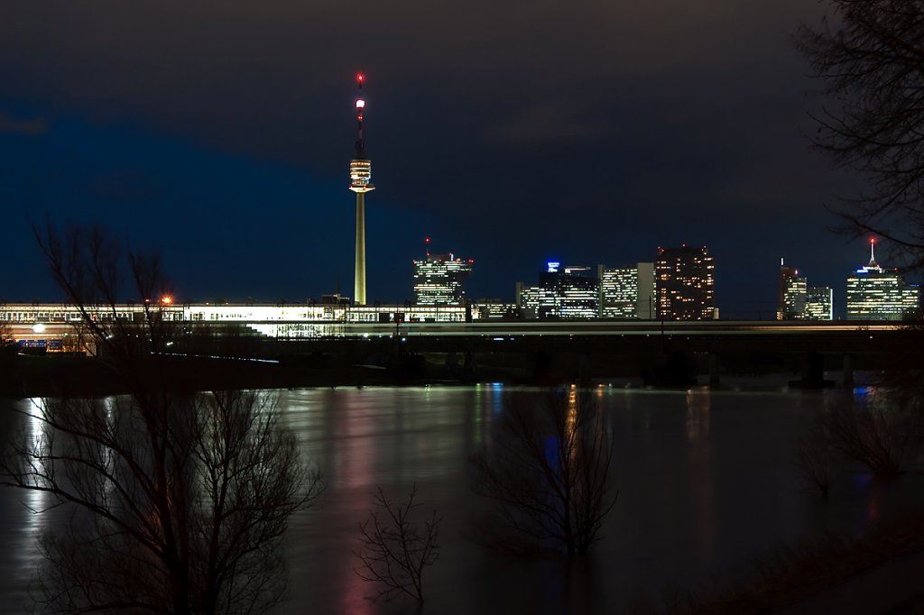 Vor der Kulisse des Wiener Donauturmes und der UNO City ist ein S - Bahnzug auf der Stammstrecke ber das Hochwasser fhrende Entlastungsgerinne unterwegs. Die Aufnahme entstand am Abend des 14.01.2011.