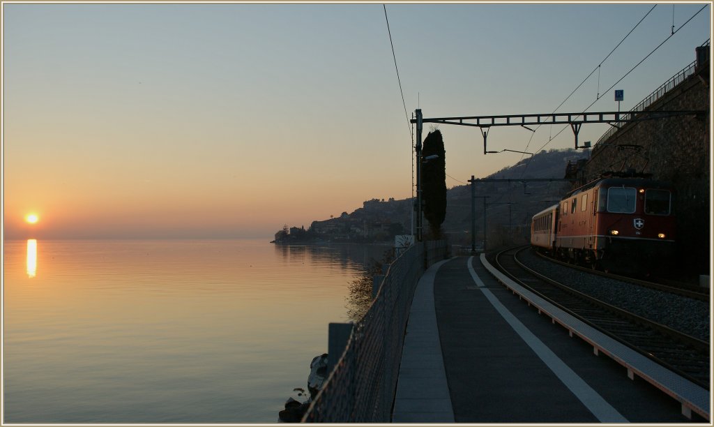Whrend die Re 4/4 II 11149 mit ihrem RE 2739 ohne Halt St-Saphorin passiert, geht im Hintergrund ber dem Lac Lman die Sonne unter. 
1. Mrz 2012