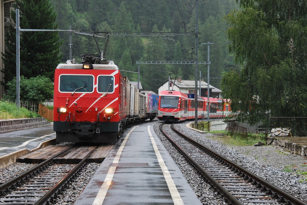 Whrend zwei Komet-Triebzge weiter fahren in die Richtung von Zermatt, fhrt eine HGe 4/4 II mit einigen Gterwagen den Bahnhof von Randa ein, 23. Juli 2011.