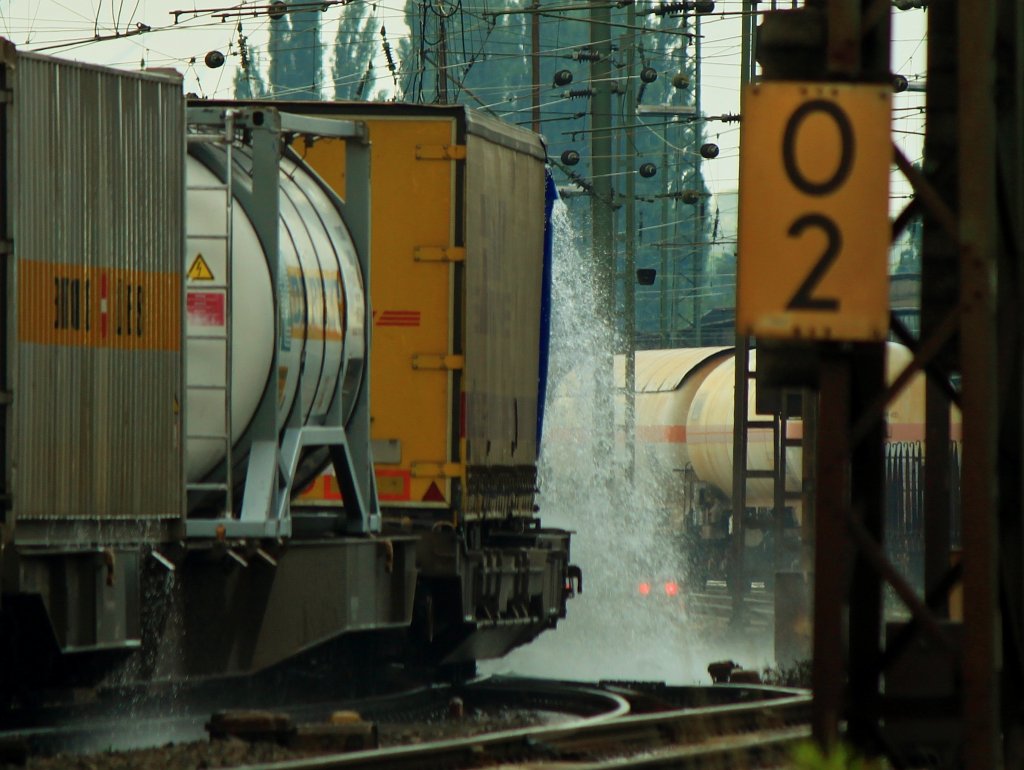 Wasserspiele 3: Bei einem heftigen Regenschauer sammelt sich Wasser auf den Planen der LKW-Auflieger, die nun an der ersten Weiche abgeschttet werden. Cobra 186 212 (2820) zieht am 10.07.2012 einen KLV-Zug aus Aachen West nach Belgien. 