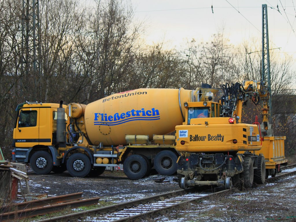Wie transportiert man Beton zu einer mitten im Gleisfeld liegenden Baustelle, die nicht mit einem Lkw angefahren werden? In Aachen West war am 11.12.2012 zu sehen wie es geht. Der Lkw l�d seine Ladung in einen kleinen Wagen, der von einem Zweiwegebagger der Firma Balfour Beatty zur Baustelle gezogen und dort abgeladen wird.