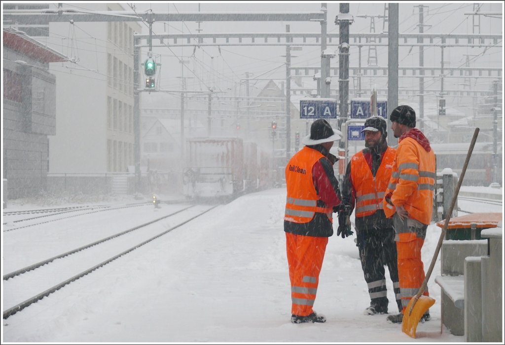 Wie wichtig Warnkleider sind ist auf diesem Bild zu erkennen. Die roten Container am Schluss des ausfahrenden RE1229 sind schon auf geringe Distanz kaum mehr zu erkennen. Die Schneerumung am Bahnhof Chur kann weitergehen. (28.01.2010)