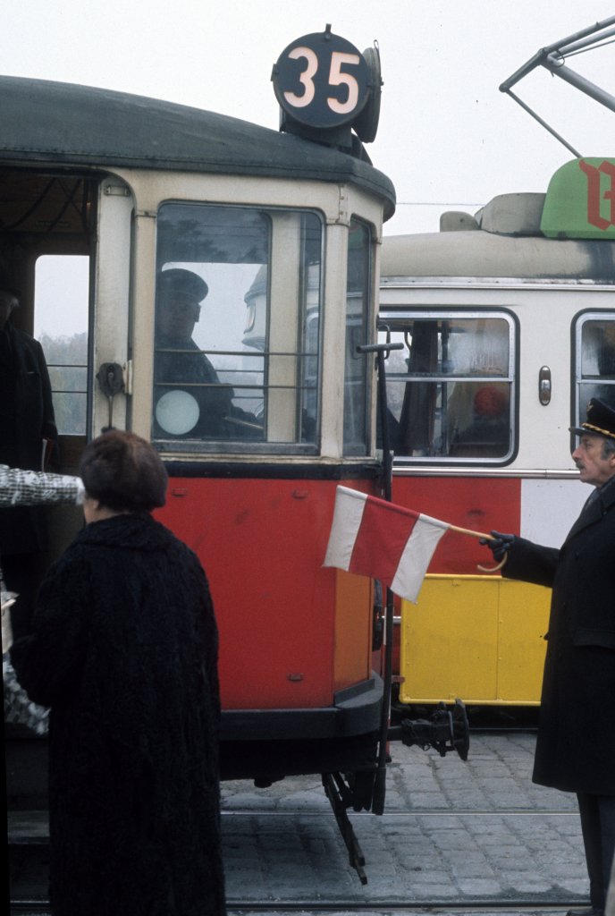 Wien Wiener Stadtwerke-Verkehrsbetriebe (WVB) Allerheiligen-Verkehr am 1. November 1975: Ein Zug der SL 35 wartet am 2. Tor des Zentralfriedhofs auf das Abfahrtsignal des Zugabfertigers. - Wegen der vielen Fahrgäste, die zu Allerheiligen den Zentralfriedhof besuchen wollten, benutzen die Verkehrsbetriebe Zugabfertiger sowohl am 2. als auch am 3. Tor des Friedhofs. - Am 1. November 1975 fuhren außer der Linie 71 und der von Gottschalkgasse / Simmeringer Hauptstraße verlängerten Linie 6 die folgenden Straßenbahnlinien zum Zentralfriedhof: 22 ab Reichsbrücke), 29(Z) ab Wexstraße, 35 ab Althanstraße / Newaldgasse) und 46(Z) ab Joachimsthalerplatz. - Scan eines Diapositivs. Kamera: Minolta SRT-101. 
