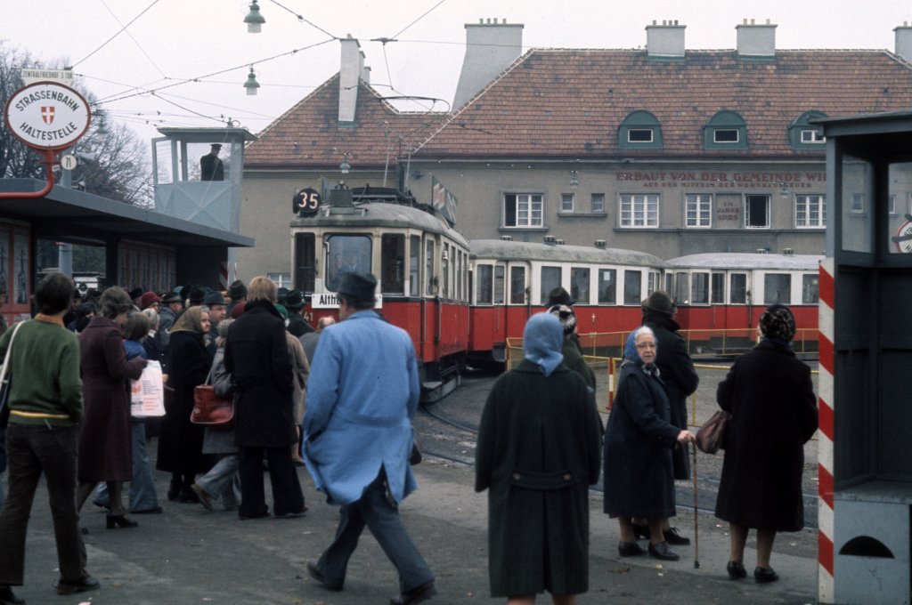 Wien Wiener Stadtwerke-Verkehrsbetriebe (WVB) Allerheiligen-Verkehr am 1. November 1975: Zentralfriedhof, Abfahrtshaltestelle am 3. Tor. - Der  Platzsprecher  im kleinen Turm links orientiert die wartenden Fahrgäste über die nächste Straßenbahnlinie. - Platzsprecher  gab es sowohl am 3. als am 2. Tor, wo sich auch die Einsatzzentrale für den Friedhofsverkehr im Expeditorturm befand. - Scan eines Diapositivs. Kamera: Minolta SRT-101.