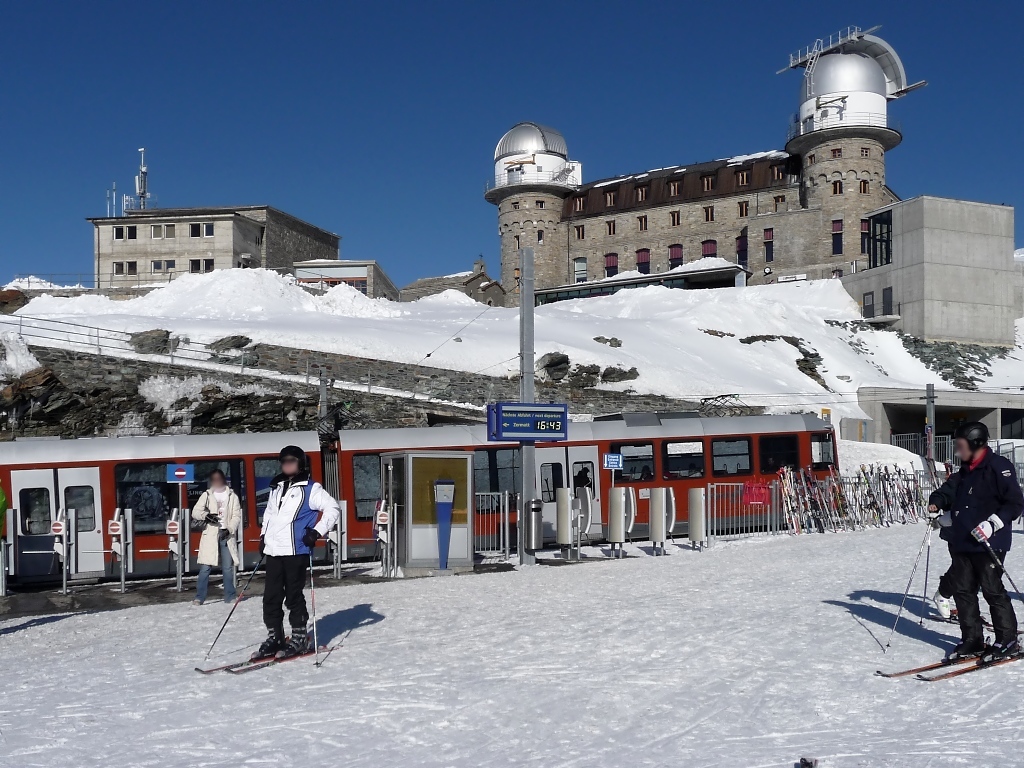 Zugang zum Bahnsteig nur durch die Bahnsteigsperren, ein eher ungewohntes Bild heutzutage (16.3.2010). Bergab ist der Zug auch zu dieser spten Zeit eher leer. 
Im Hintergrund das Observatorium auf dem Gornergrat in 3135 Metern Hhe.