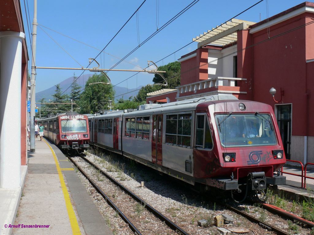 Zugkreuzung bei der Circumvesuviana in Pompei-Scavi. Im Vordergrund fhrt eine Dreifachkompostion aus ETR035+ETR015+ETR095 von Napoli nach Sorrento.
Im Hintergrund grt (und droht stets auch) der Vesuv.

2010-08-24 Pompei-Scavi