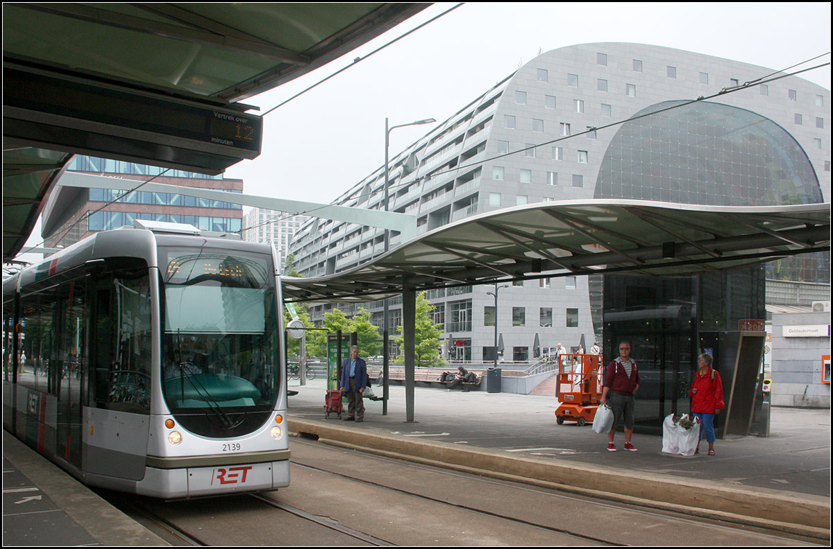 . Bogen nach unten/Bogen nach oben -

Citadis-Tram und Markthalle in Rotterdam. 

Wer mal nach Rotterdam kommt sollte unbedingt einen Blick in die neue Markthalle an der Haltestelle Blaak werfen. Die 2014 eröffnete Markthalle der Rotterdamer Architekten MVRDV besteht aus einer hohen Halle mit ovalförmiger bunt bemalter Decke. Der Querschnitt dieser halle entspricht der rechts sichtbarer Glasfassade. An den Längsseiten befinden sich Wohnungen.

An der Tram Haltestelle Blaak kann zur hier unterirdisch verlaufenden Bahnlinie umgestiegen werden. Daher wurde auch die Straßenbahnhaltestelle architektonisch aufwändiger gestaltet.

21.06.2016 (M)

