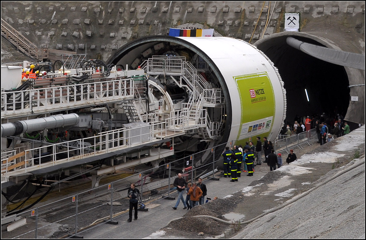 . Der  Bohrkopf  - 

Zwischen dem Schneiderad vorne und dem Ende des runden Metal-Schildes entsteht der Tunnel. Das über 10 Meter im Durchmesser große Schneiderad beißt sich durch das Gestein, während im hinteren teil des Schildes schon die Innenschale des Tunnel mit Betonfertigteilen (Tübbings) gebaut wird. Jeweils am zuletzt gebauten Tübbing-Rind schiebt sich die Maschine mit Pressen nach vorne. Im Nachläufer wird oben der Aushub nach hinten transportiert, während im unteren Bereich die Tübbings nach vorne gebracht werden.

Aufnahme am Tag der Offenen Baustelle am 10.07.2014 (Jonas)
