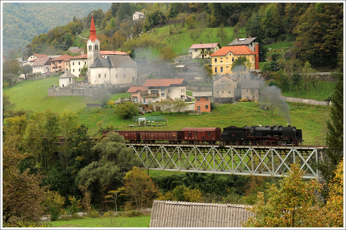 06-018 mit ihrem 17032 von Nova Gorica nach Jesenice, am 10.10.2015 kurz nach der Ausfahrt aus dem Bahnhof Grahovo mit Blick auf Grahovo ob Bači.