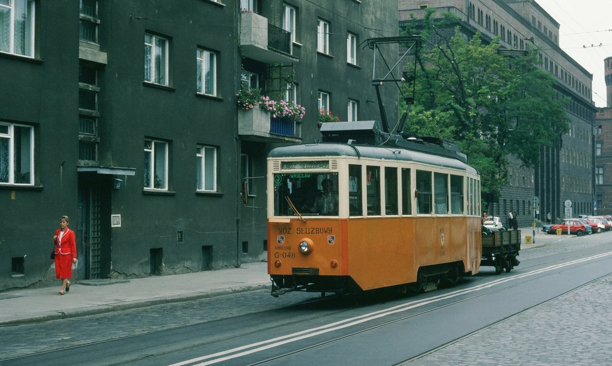 09.08.1993, Polen, Wroclaw/Breslau: Ein Arbeits-Tw fährt vorüber. Die rote Dame peppt das graue Haus ein wenig auf.