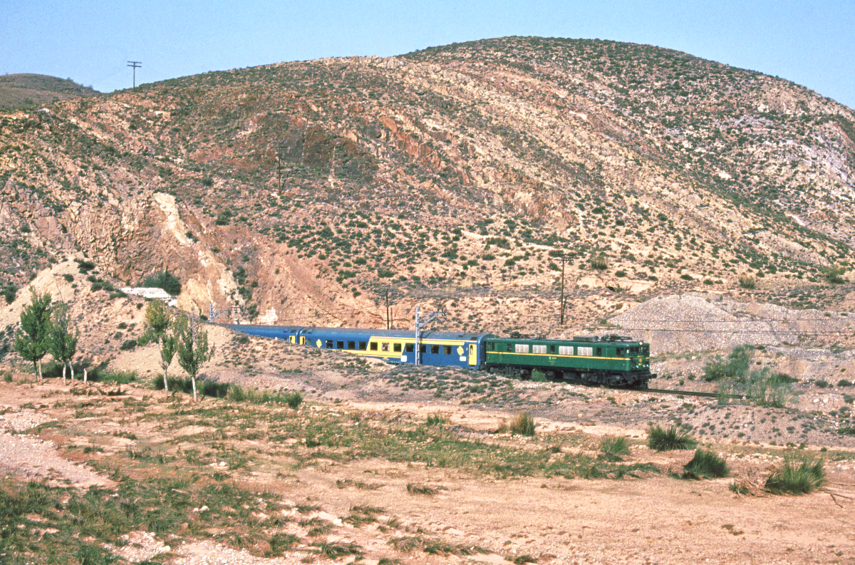 10 Stunden war der Rapido 575 von Barcelona (7.55) nach Madrid (17.57) planmäßig unterwegs. Zwischen Sitges bei Barcelona und Guadalajara bei Madrid hielt er an allen Bahnhöfen. Hier sehen wir ihn kurz vor Calatayud (Zaragoza), welches er um 14.35 erreicht. Es führt eine  Japonesa  der Baureihe 269. Calatayud, Oktober 1983. Canon AE1, digitalisiert mit Canoscan, bearbeitet mit GIMP.