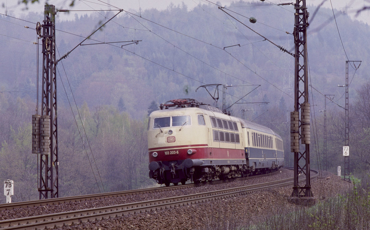 103 203 hat mit einem IC gerade den Schwarzkopftunnel verlassen und  fährt auf der Spessart-Westrampe talwärts Richtung Aschaffenburg. 
Das Bild entstand 1986 - die alte Spessartrampe ist zwischenzeitlich zurückgebaut, der Schwarzkopftunnel ist verfüllt und die Züge befahren heute dort eine vollständig neu trassierte Strecke mit deutlich geringerer Neigung.