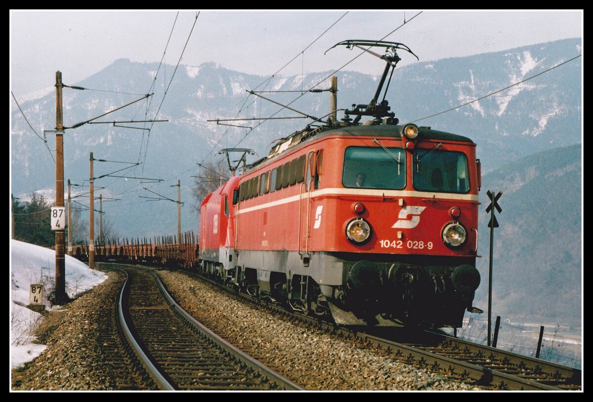 1042 028 bringt gemeinsam mit 1116 172 einen Güterzug über die Nordrampe des Semmerings. Das Bild entstand kurz vor dem Bahnhof Eichberg am 13.03.2004. Damals gab es noch Linksverkehr auf der Semmeringbahn, seit ca. zwei Jahren wurde das auf Rechtsverkehr geändert.