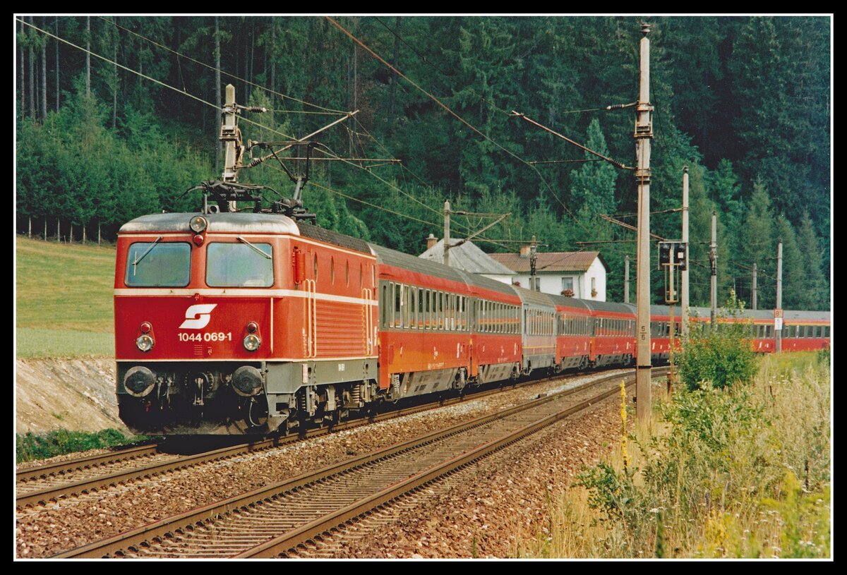 1044 069 fährt am 4.08.1994 mit EC31 (Wien Süd - Rom) bei Leoben Hinterberg durchs Murtal. Durch den Bau des Galgenbergtunnels (eröffnet 1998) konnte dieser Streckenabschnitt aufgelassen werden.