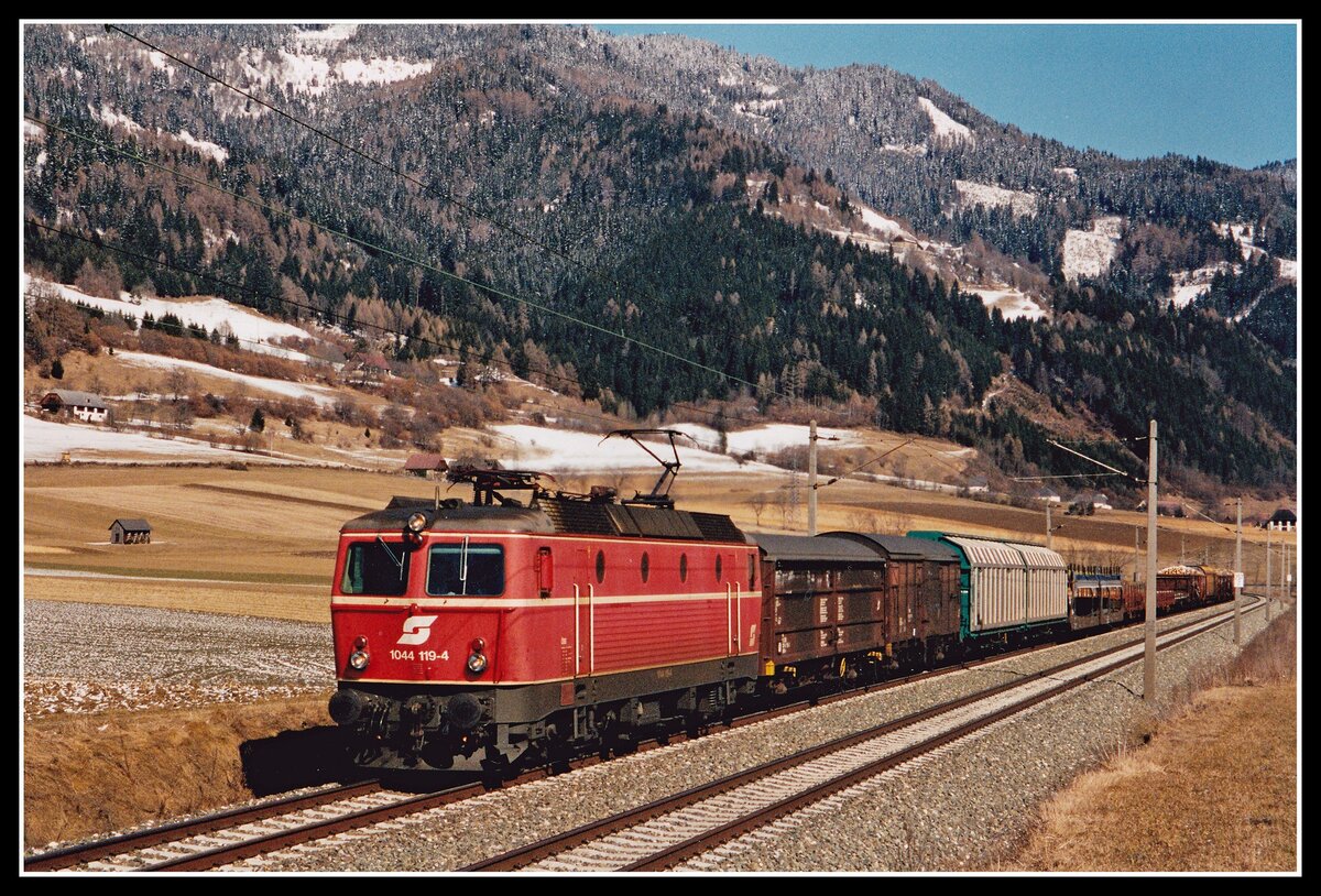 1044 119 ist mit G53507 (Ferngüterzug von Wien Zvbf. nach Villach Süd) im Murtal unterwegs und erreicht in Kürze den Bahnhof Unzmarkt. Das Bild entstand am 27.02.2001.