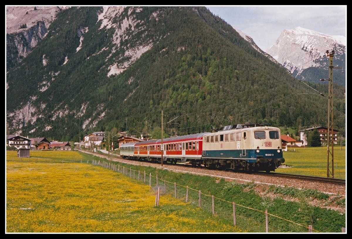 110 243 fährt am 6.05.2002 mit R5421 durch blühende Wiesen bei Scharnitz . Die Berge im Hintergrund gehören alle zum Karwendelgebirge.