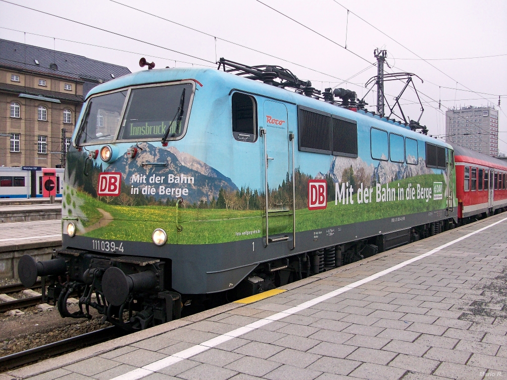 111 039 mit Werbung für den Deutschen Alpenverein und einem aus n-Wagen bestehenden Regionalzug nach Innsbruck warten am Morgen des 5.4.2013 in München Hbf auf die bevorstehende Abfahrt.