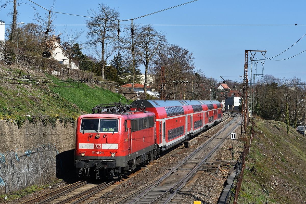 111 050, die mit Scherenstromabnehmern unterwegs ist, bespannt am 29. März 2019 einen RE nach Lindau bis Ulm Hbf. Hier passiert der Zug den Syrlinsteg in Ulm kurz vor dem Hauptbahnhof.