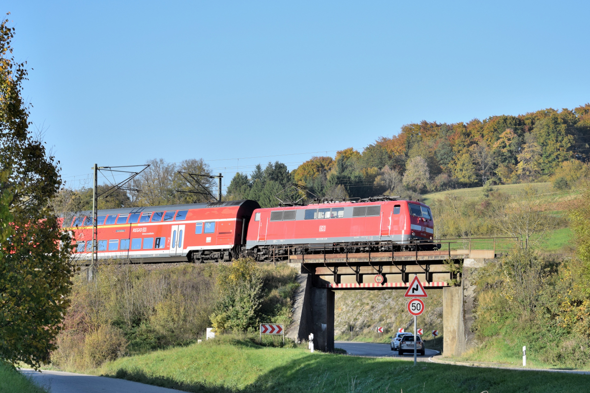 111 058 hat am 14.10.2017 bereits die Geislinger Steige bezwungen und strebt nun mit ihrem IRE nach Lindau Ulm entgegen, wo auf eine Diesellok umgespannt wird. Hier überquert sie die B10 in Urspring.