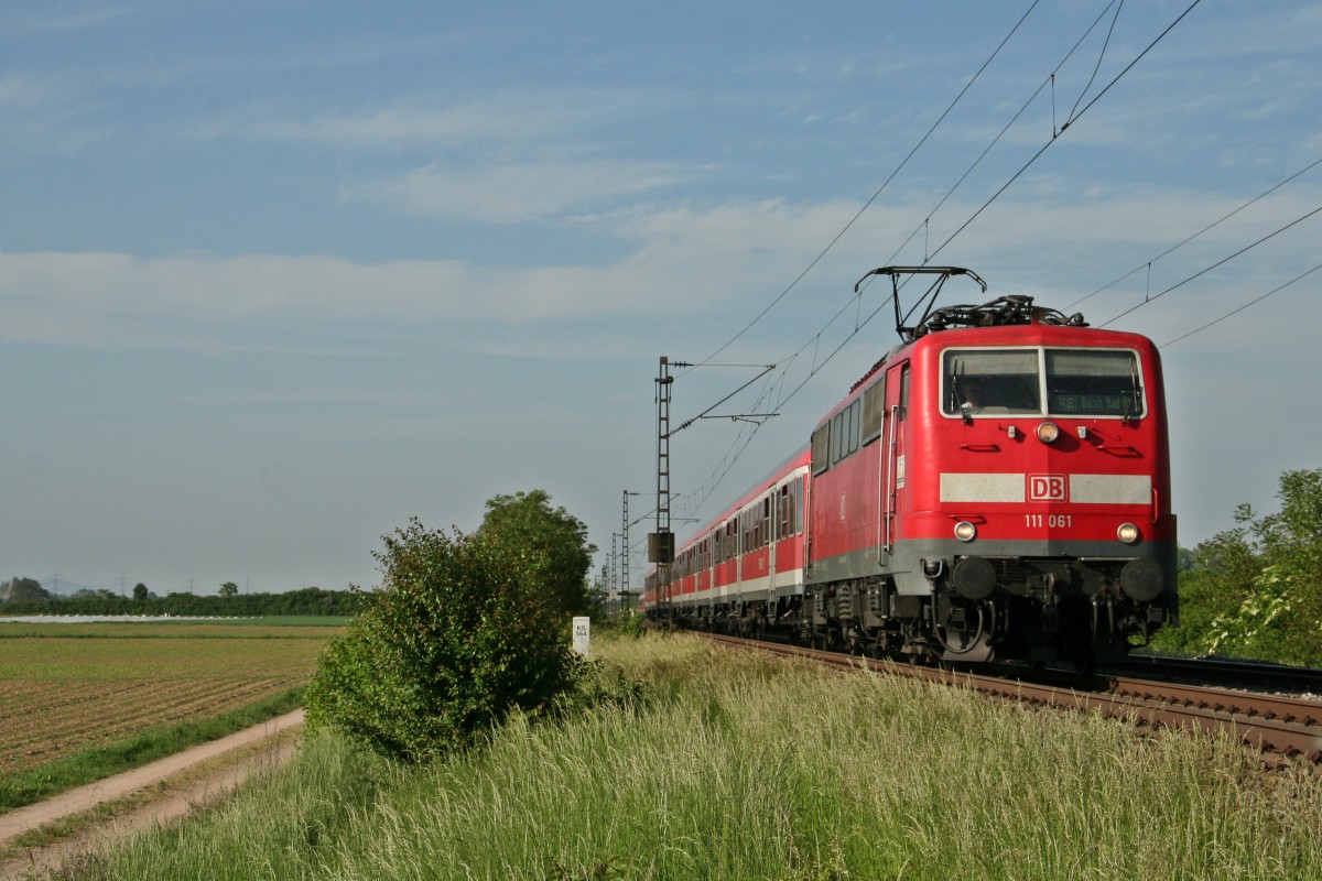 111 061 mit einer RB von Offenburg nach Basel Bad. Bf am Nahcmittag des 13.05.15 bei Hgelheim kurz vor dem Bahnhof Mllheim (Baden), wo sie den nchsten Halt einlegen wird.
