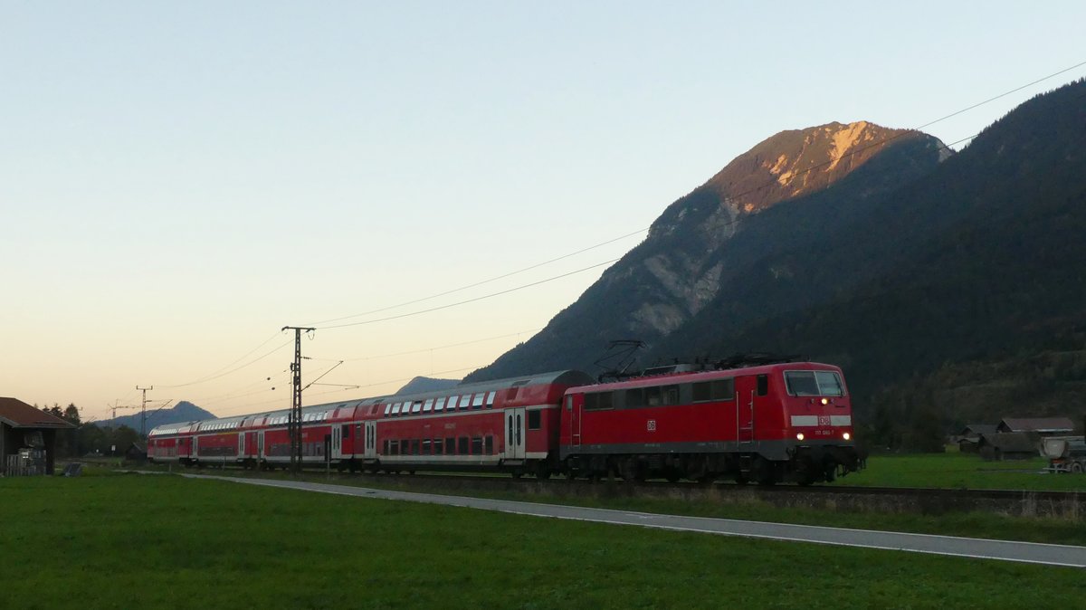 111 066 zieht den Verstärker-RE nach Mittenwald im schwindenden Licht über die Felder zwischen Farchant und Garmisch-Partenkirchen. Aufgenommen am 10.10.2018 18:10