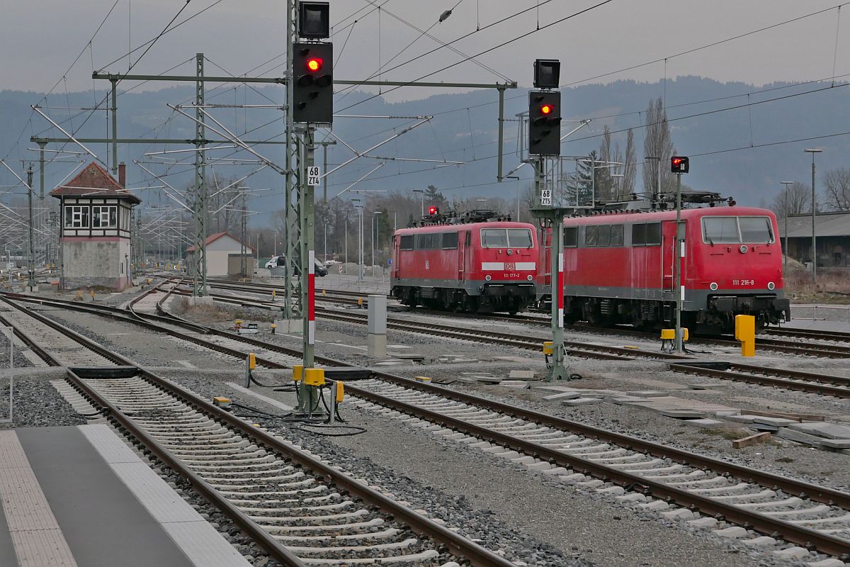 111 177-2 und 111 216-8 am 17.03.2022 in Lindau-Reutin. Mit im Bild das Gebäude des ehemaligen Stellwerkes 'Lrm'.