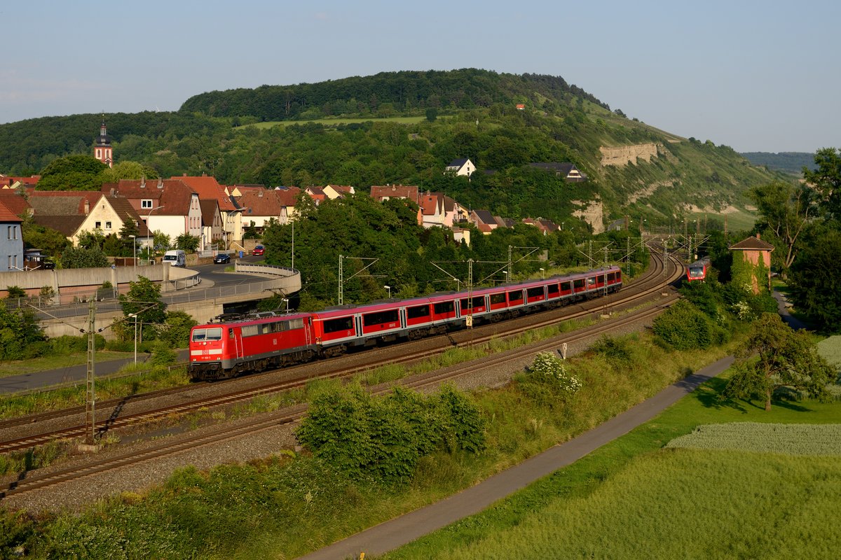 111 186 erreicht am Abend des 17. Juni 2013 mit ihrem aus den sogenannten PUMA-Wagen gebildeten RE 4624 den Bahnhof Retzbach-Zellingen. Im Hintergrund stiehlt sich gerade ein Mops als RB 58073 gen Würzburg aus dem Bild.