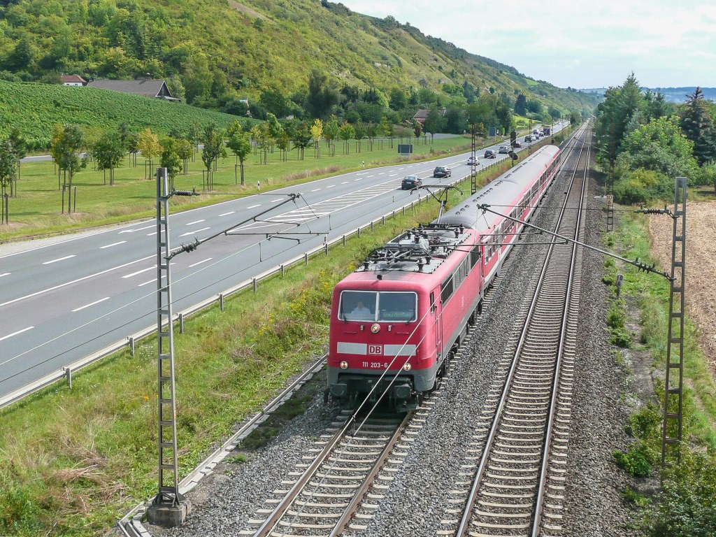 111 203 zog am 12.8.09 vier Bn-Wagen als RB nach Gemünden. Links die Bundesstraße B8, rechts vom Bildrand fließt der Main.