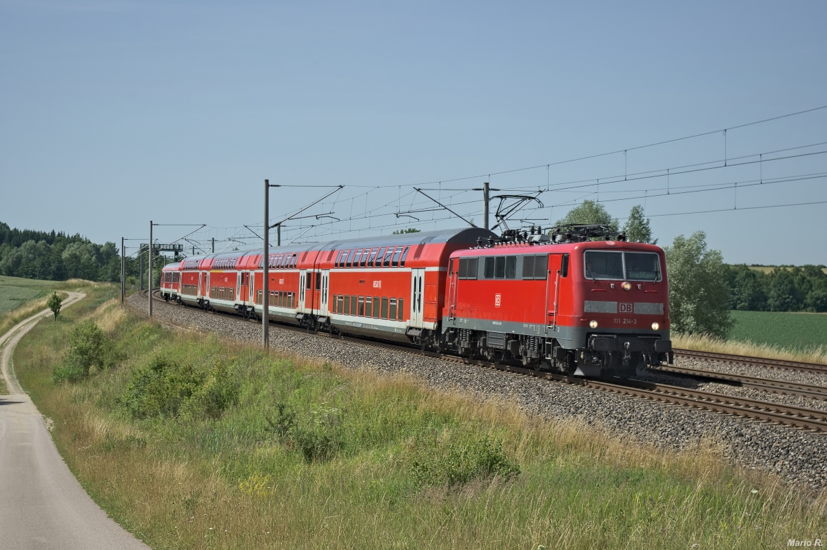111 214 verkehrte am 4.7.2014 als RB 59150 von München nach Nürnberg und konnte bei Asbach kurz vor dem Halt Petershausen (Obb.) aufgenommen werden. Bis zum Ende des Verkehrsvertrages 2016 (und darüber hinaus) verkehrten auf der KBS900 neben vollständigen Doppelstockgarnituren auch Kamel-Züge. Züge, die aus Doppelstockwagen und Wittenberger Steuerwagen gebildet wurden. Um einen solchen  Kamel-Zug  handelt es sich hier.