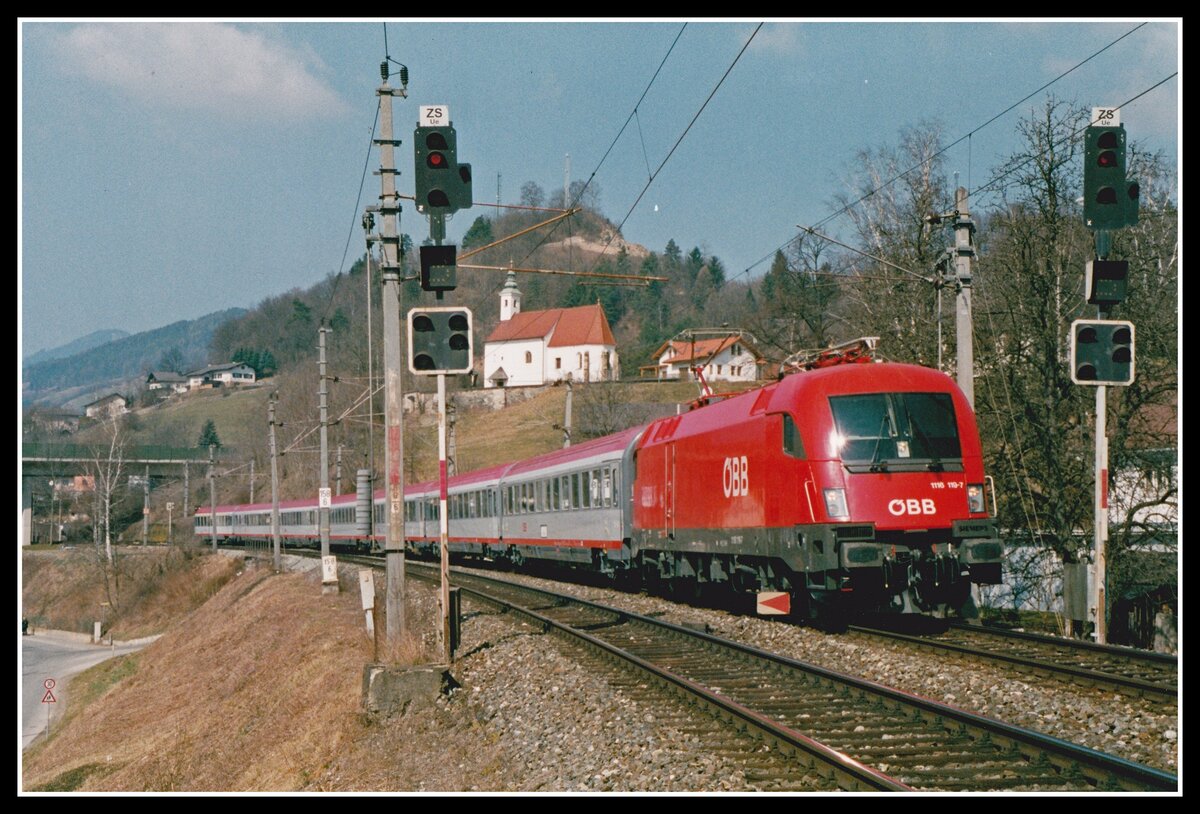 1116 119 mit EC555 ist am 18.03.2003 kurz nach Bruck an der Mur unterwegs. Über dem Zug sieht man die Nikolauskirche.