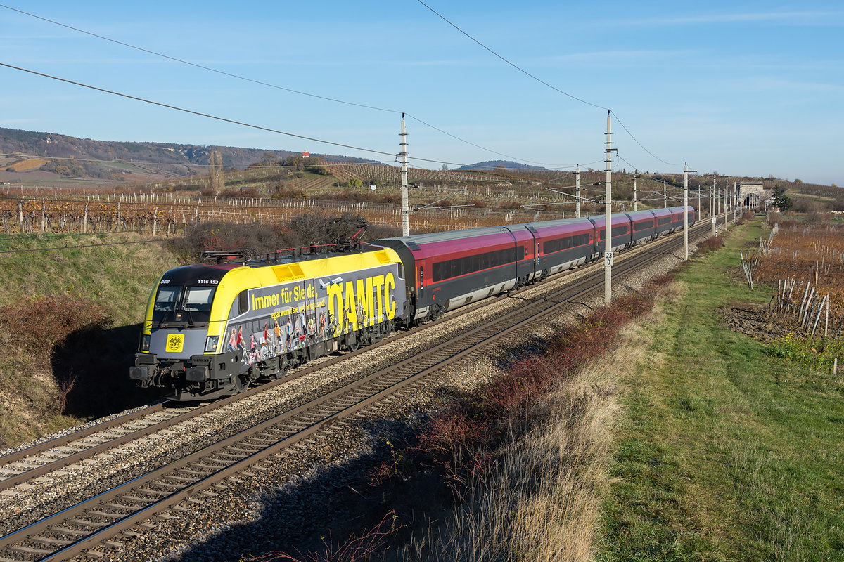 1116 153 im neuen ÖAMTC Look, war am 22.11.2020 mit dem railjet 559 von Wien Flughafen nach Graz Hbf. unterwegs. Die Aufnahme entstand bei der Fahrt durch die spätherbstlichen Weingärten zwischen Gumpoldskirchen und Pfaffstätten.