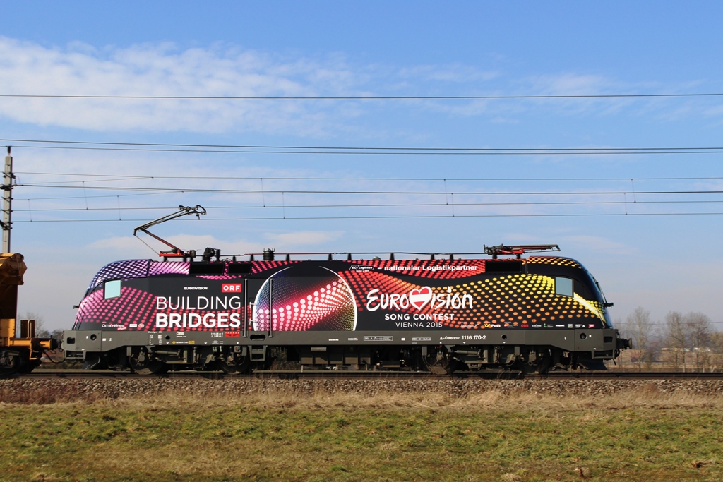 1116 170-2  Eurovision Song Contest  mit einem Güterzug vor der Haltestelle Oftering Richtung Linz am 21.2.2015