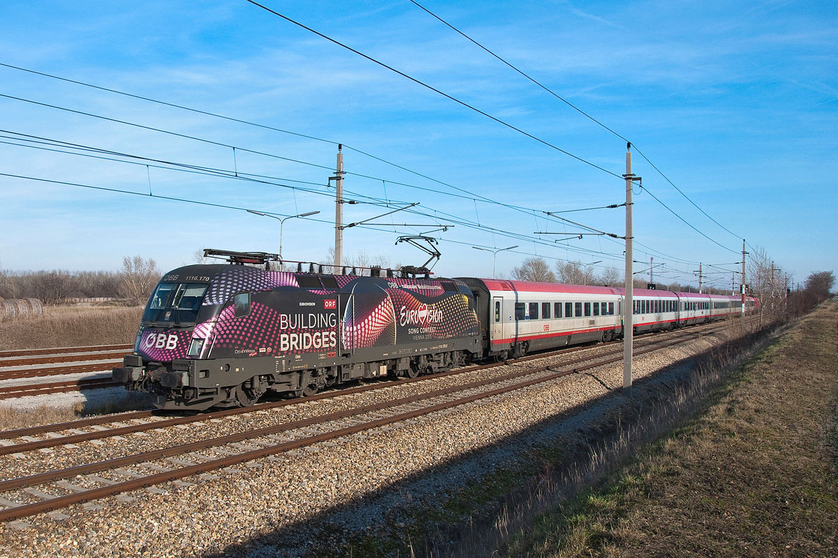 1116 170  Eurovision  ist mit dem IC 692 in Richtung Wien Hbf. unterwegs. Die Aufnahme entstand am 06.02.2016 zwischen Wien Flughafen und Mannswörth.