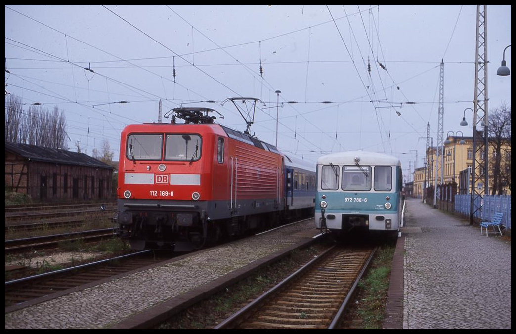 112169 hält am 8.11.1998 um 14.15 Uhr mit dem Interregio nach Nürnberg im Bahnhof Wittenberge. Daneben steht schon eine modern lackierte Ferkeltaxe 972768 als Anschluss Bahn.