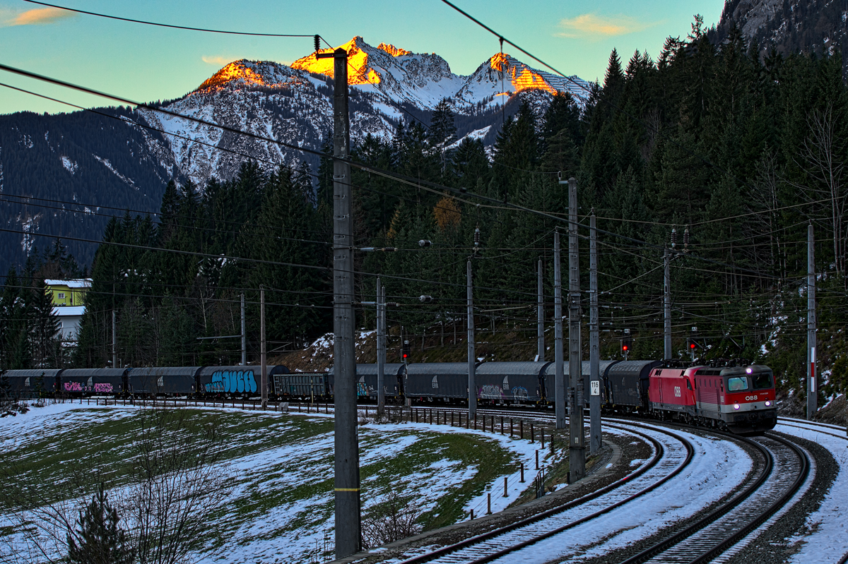 1144 028 und eine 1116 fahren bei Sonnenaufgang im Klostertal mit einem Stahlzug in Wald a/A vorüber.Bild vom 4.12.2015