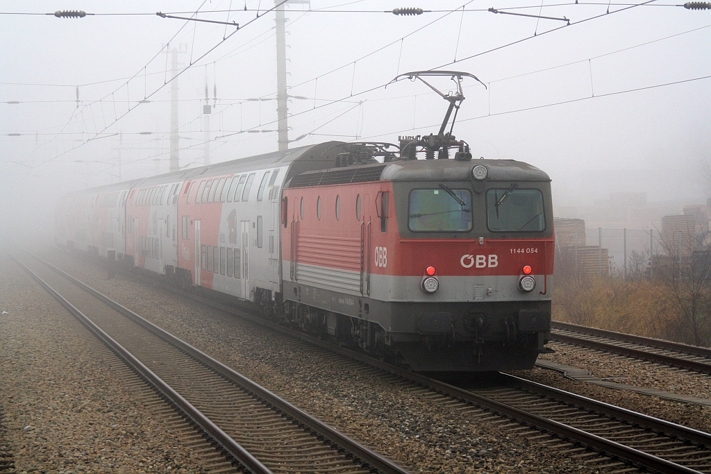 1144 054-4 schiebt am 19.Dezember 2015 im dichtem Nebel den R 2330 durch Brunn-Maria Enzersdorf Nord in Richtung Wien. Aufgenommen von der Plattform des letzten Wagen des SR 14051.