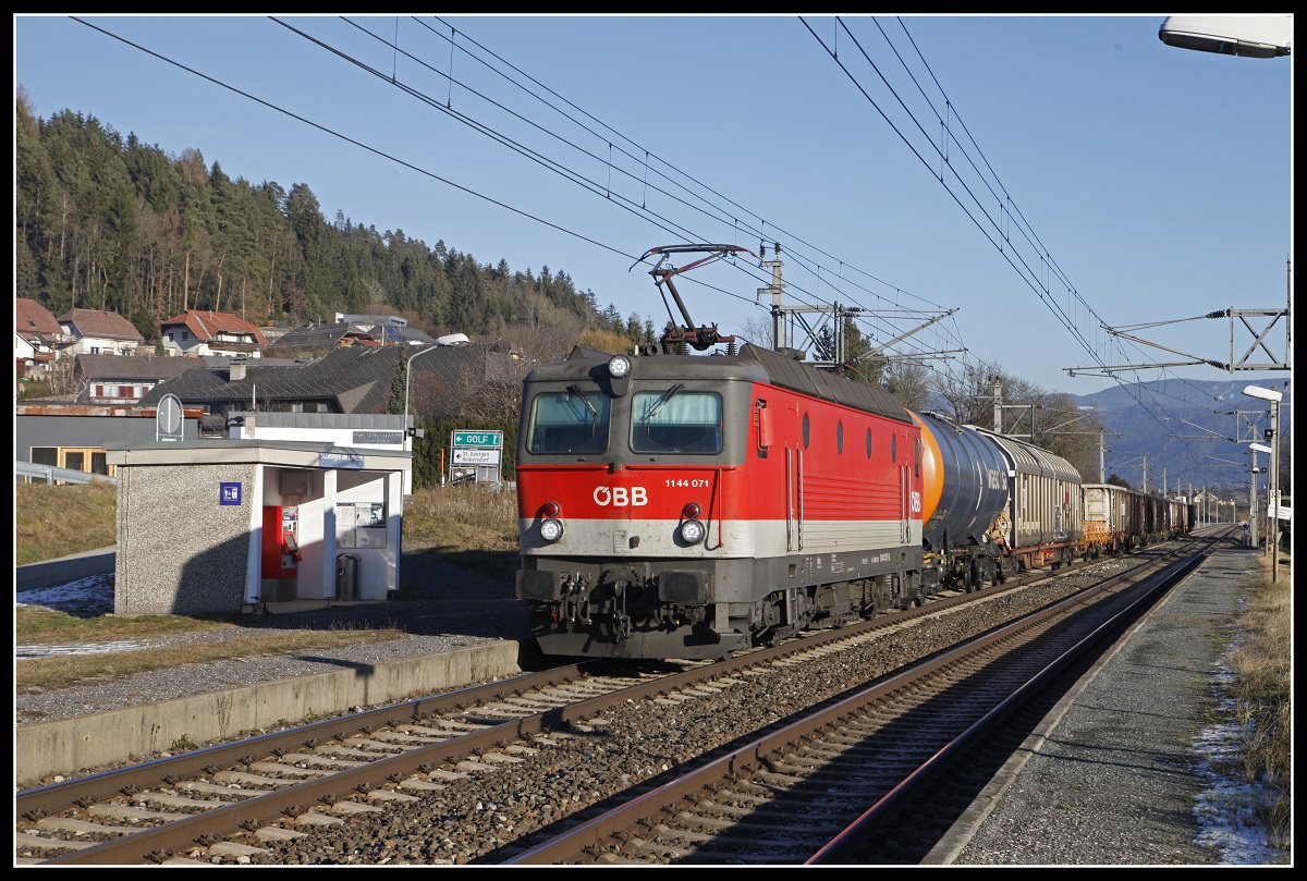 1144 071 fährt am 18.12.2018 mit einem Güterzug durch die Haltestelle St.Georgen am Längsee.
