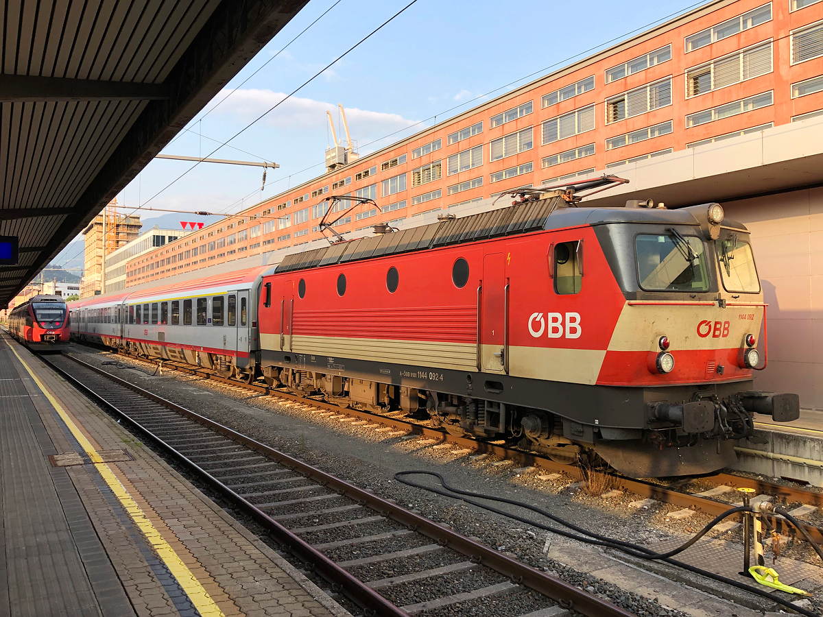 1144 092-4  Schachbrett  in den ersten Sonnenstrahlen mit REX 5361 nach der Ankunft aus Gleis 1 von Landeck-Zams. Aufgenommen am frühen Morgen des  22.07.2021 in Innsbruck Hbf